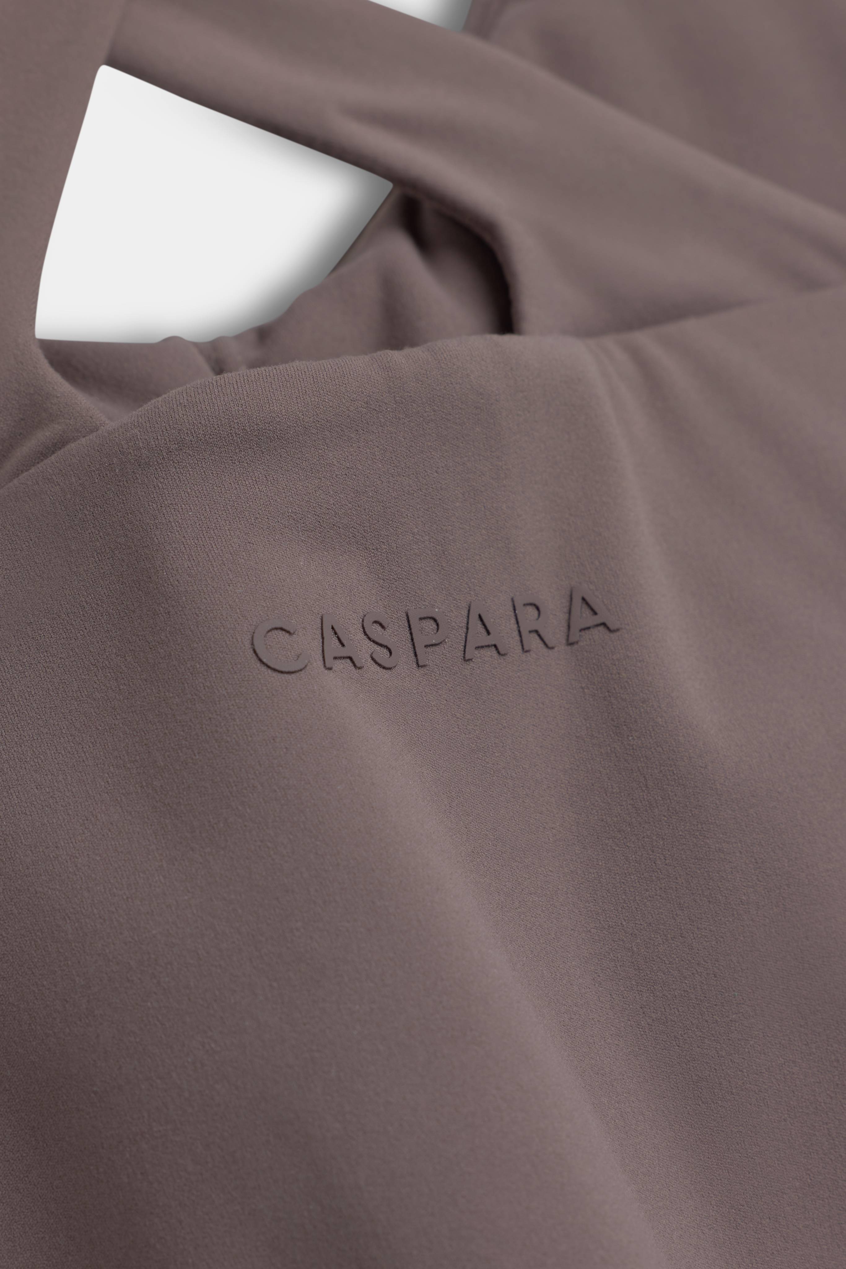 Close-up of the embossed CASPARA logo on a walnut brown Cloudform Scrunch Top.